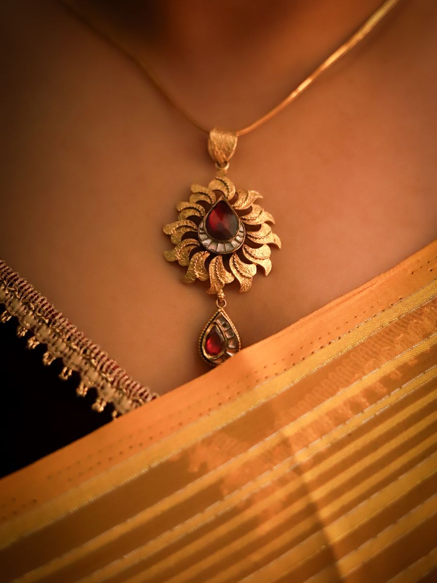 Gold pendant with a red gemstone displayed on traditional red fabric