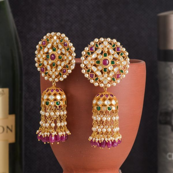 Gold earrings with pearls and gemstones displayed on a clay pot